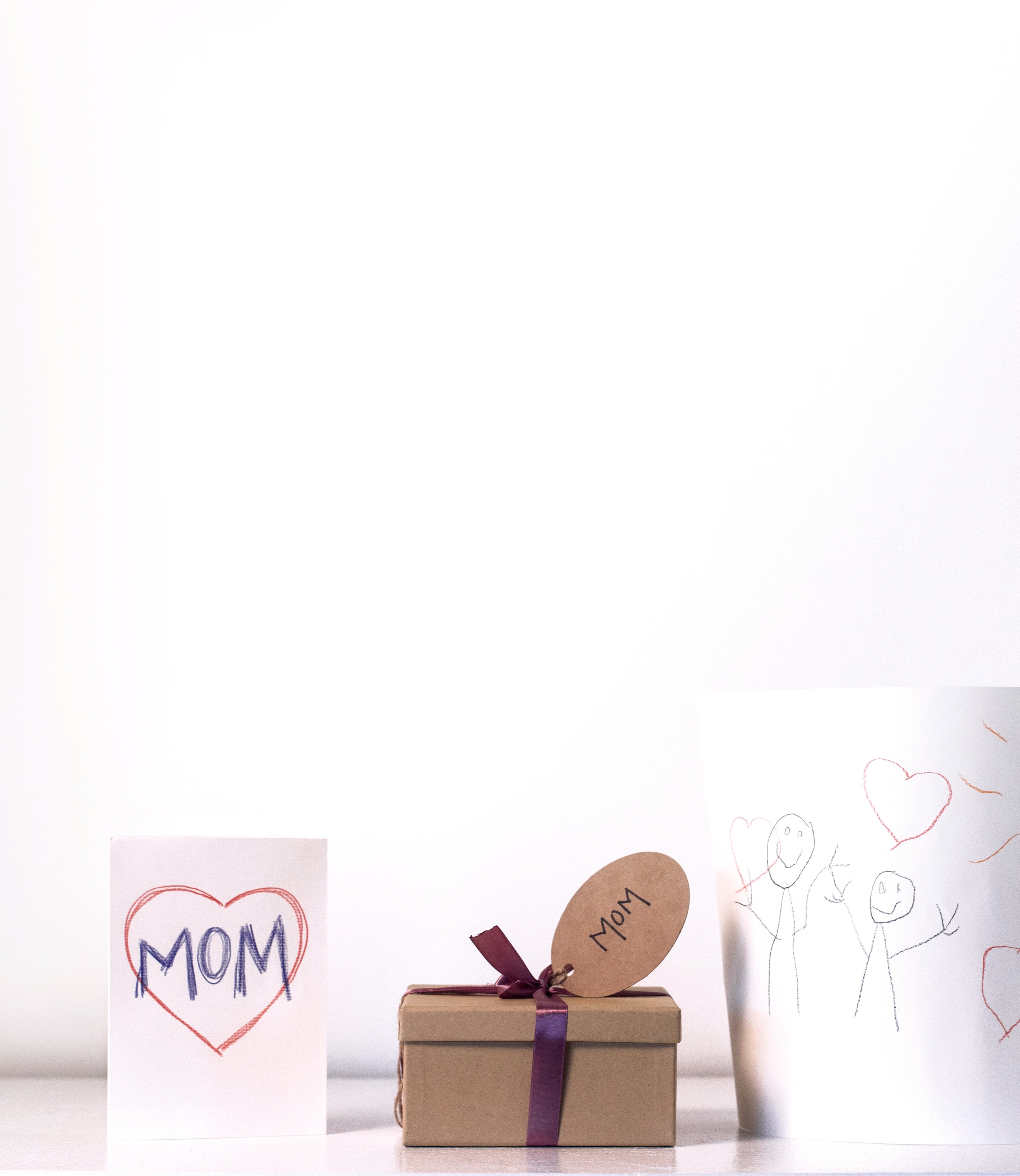 Small gift box with a heart-shaped tag and a card with 'Mom' on it, on a white background.