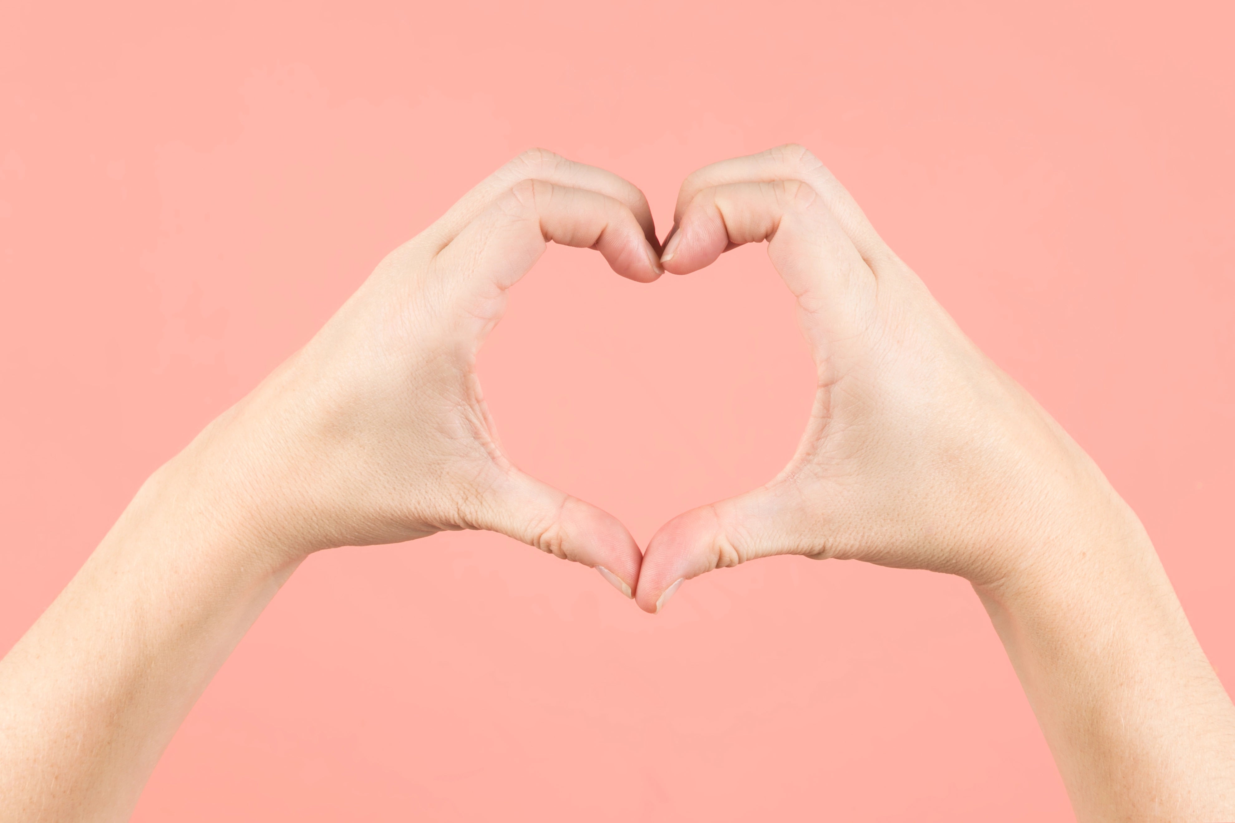 Hands forming a heart shape on a pink background