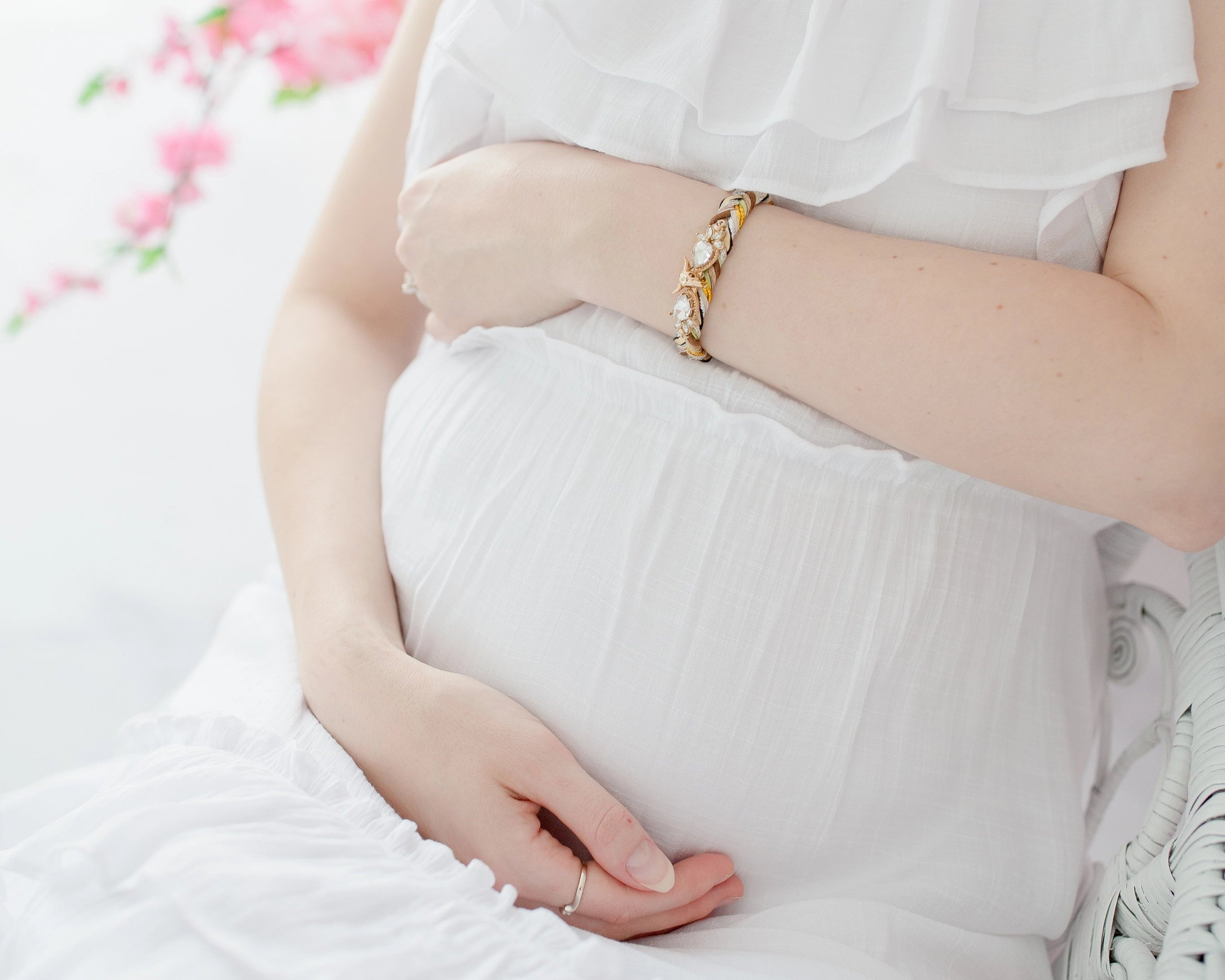 Pregnant woman in a white dress holding her belly with a soft, blurred floral background